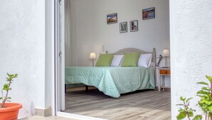 Un dormitorio con cama, almohadas, mesita de noche, lámpara y una pared con cuadros.