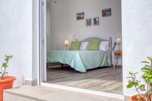 Un dormitorio con cama, almohadas, mesita de noche, lámpara y una pared con cuadros.