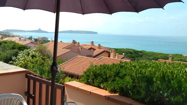 A terrace with a table, an umbrella, and a view of the sea and buildings.