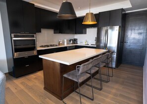 Eine moderne Küche mit einer zentralen Kochinsel, Barhocker, einem Backofen und einem Edelstahlkühlschrank.