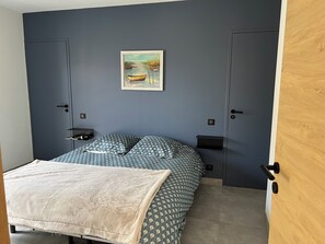 A bedroom with a bed, a bedside table, a nightstand, a wall-mounted painting, and a wardrobe. - Bright, quiet house near the beach. (Saint-Lunaire)