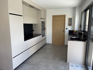 A modern kitchen with white cabinetry, a black countertop, and a wooden door. - Bright, quiet house near the beach. (Saint-Lunaire)