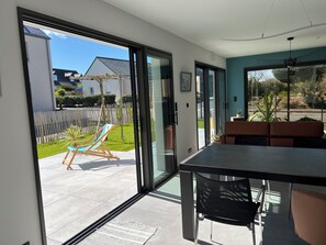 A modern room with a sliding glass door leading to a patio, a dining table, and a sofa. - Bright, quiet house near the beach. (Saint-Lunaire)