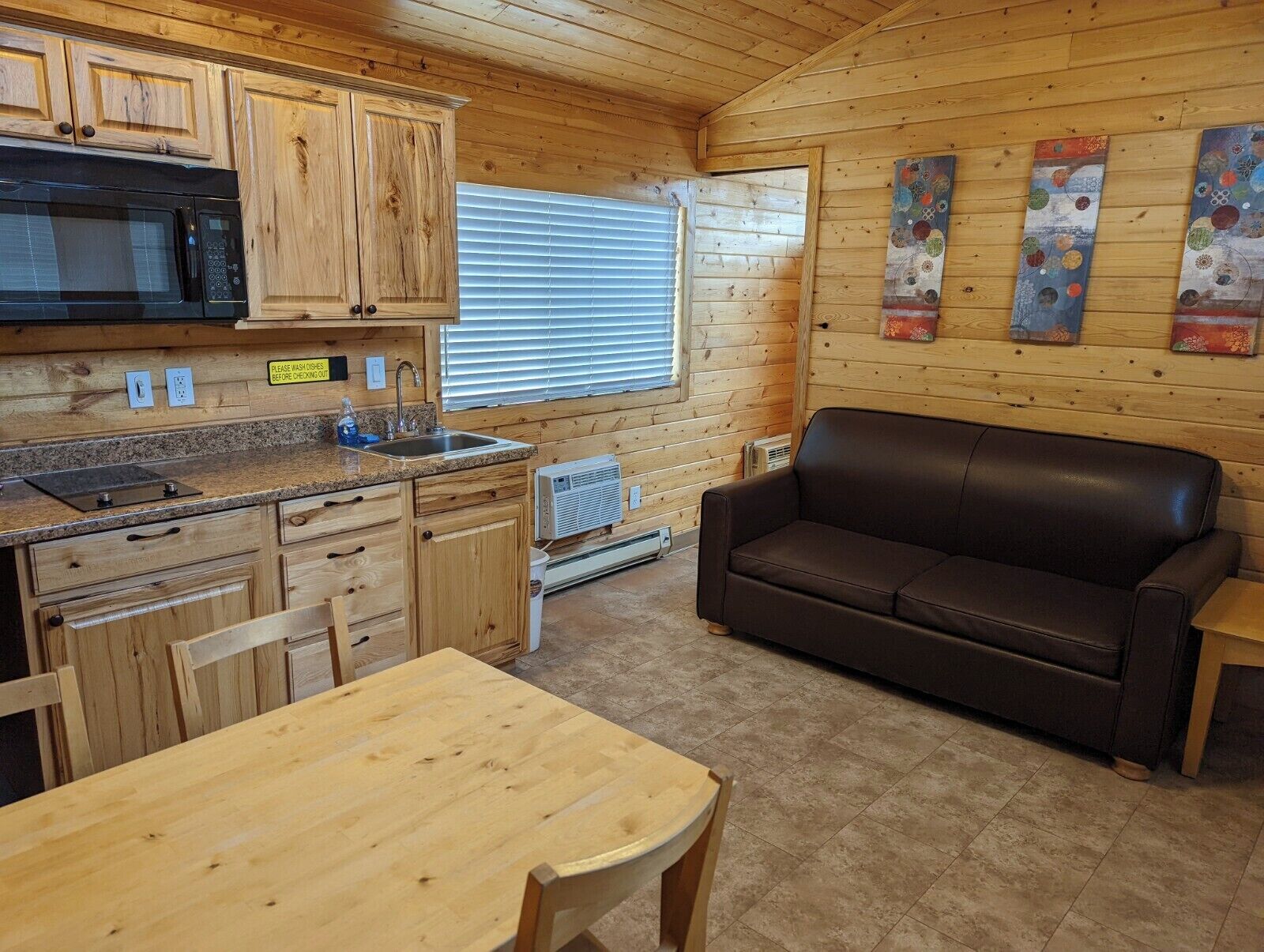 A wooden cabin interior with a kitchen, dining table, and a brown leather couch.