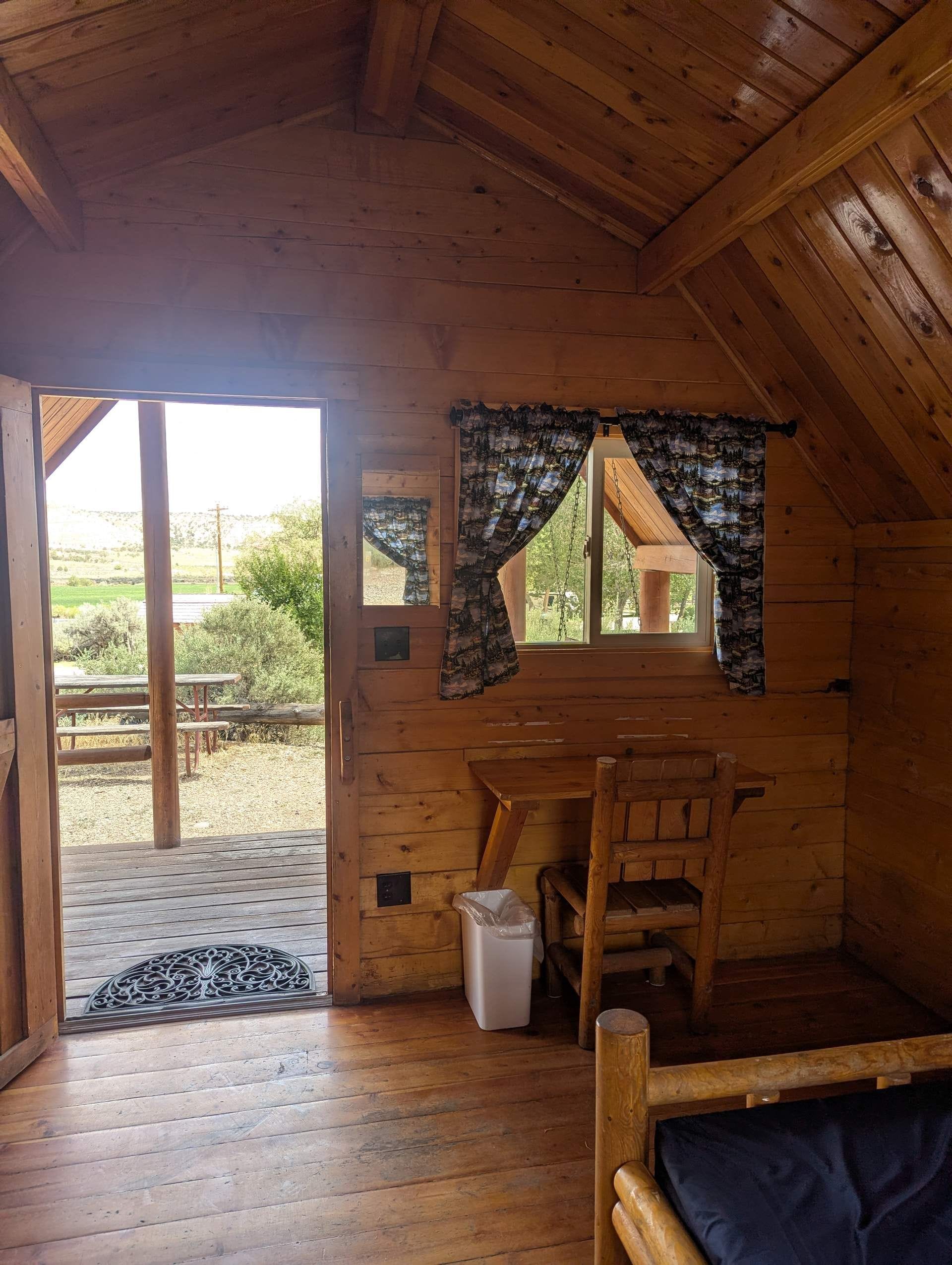 Interior de una cabaña de madera con una mesa de comedor, sillas, un banco y vistas al exterior.