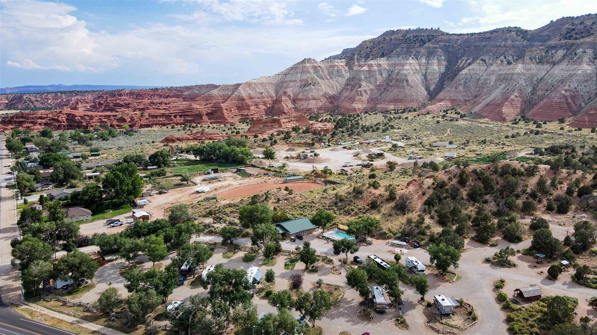Vista aèria d'una zona rural amb un petit assentament, incloent cases, autocaravanes i un camí de terra.