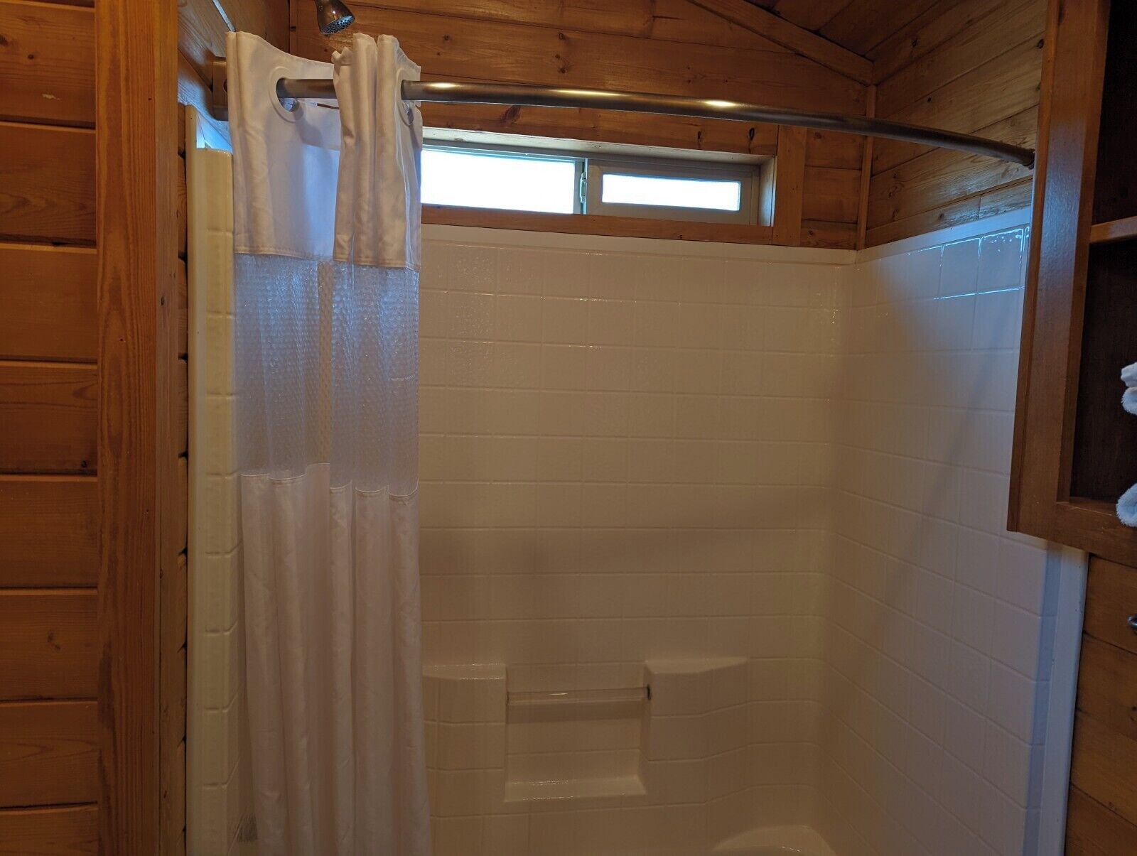 A shower area with a wooden ceiling and white tiled walls.