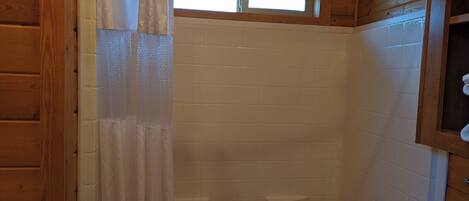 A shower area with a wooden ceiling and white tiled walls.