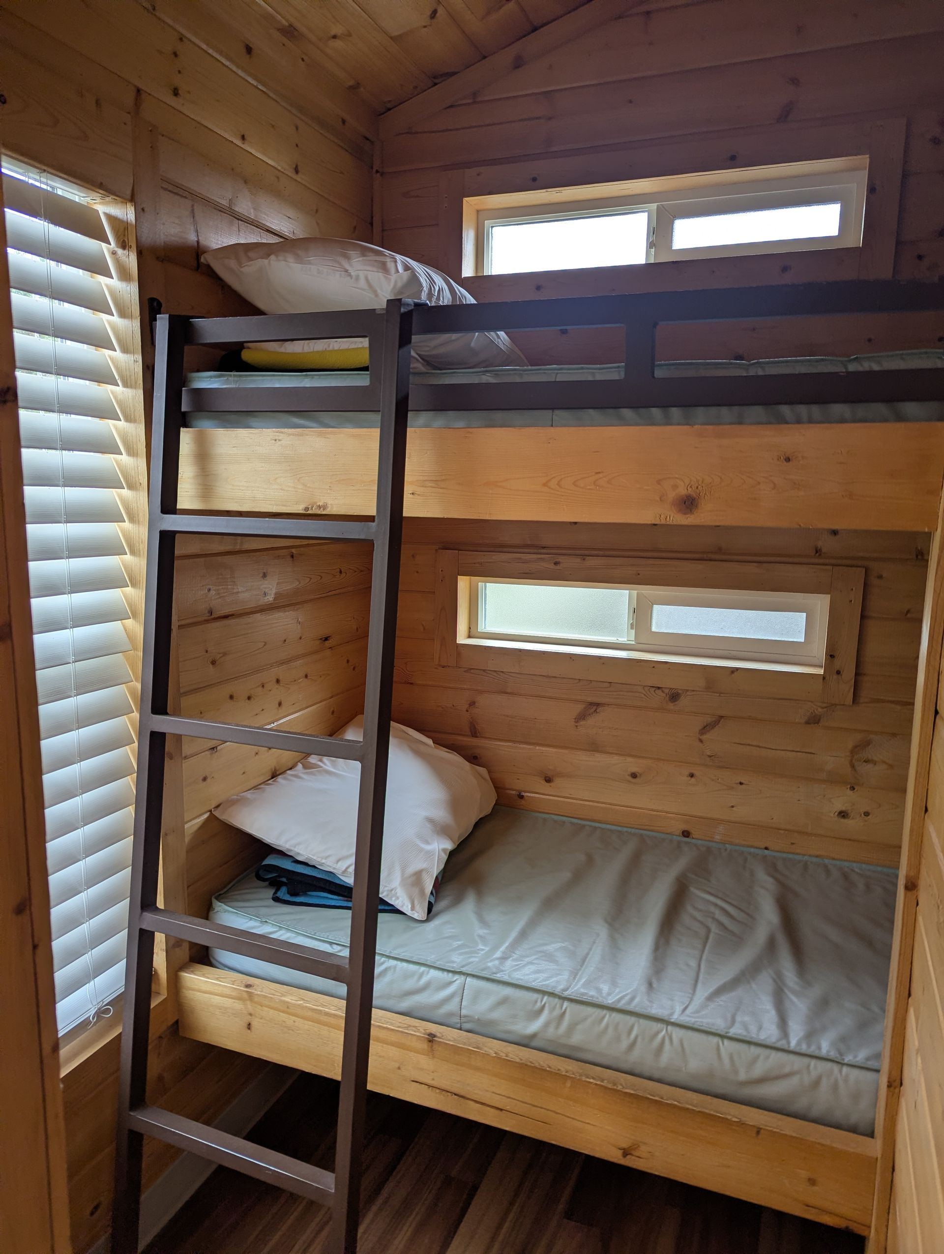 Een stapelbed met een ladder, twee ramen en een houten interieur.