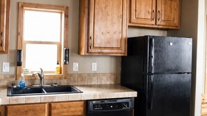 A kitchen with wooden cabinets, a black refrigerator, and a dishwasher. - Bryce Canyon RV Resort (Cannonville)
