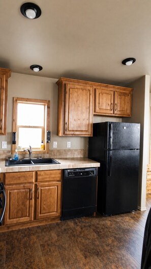Una cocina con armarios de madera, un refrigerador negro y un lavavajillas.