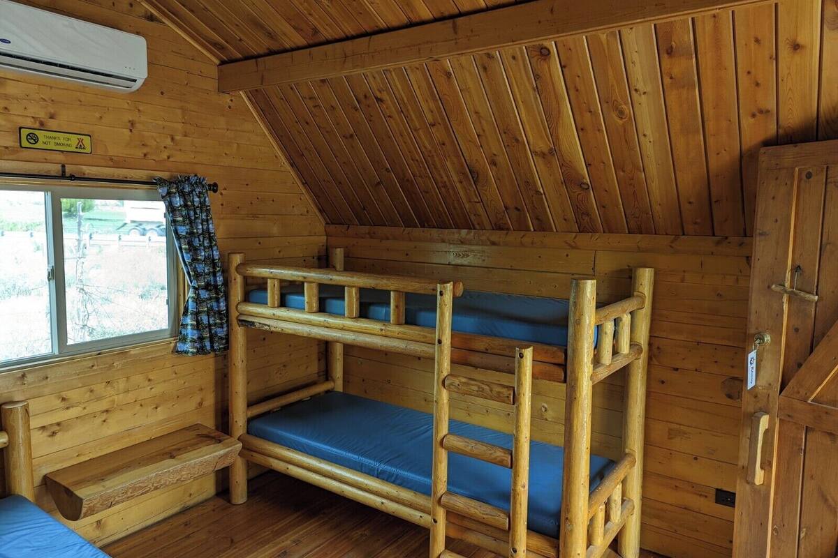 A cabin with a loft bed, a bench, and a window with curtains.