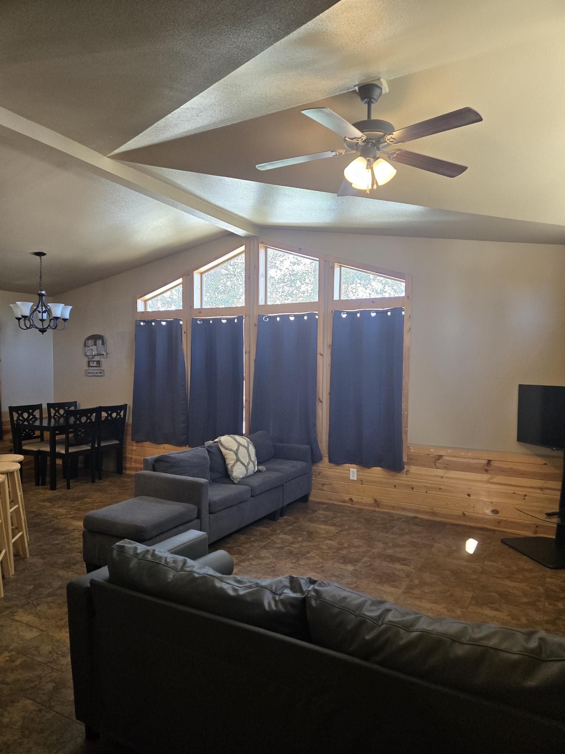 A living room with a ceiling fan, a sofa, a loveseat, a dining table with chairs, and a TV.