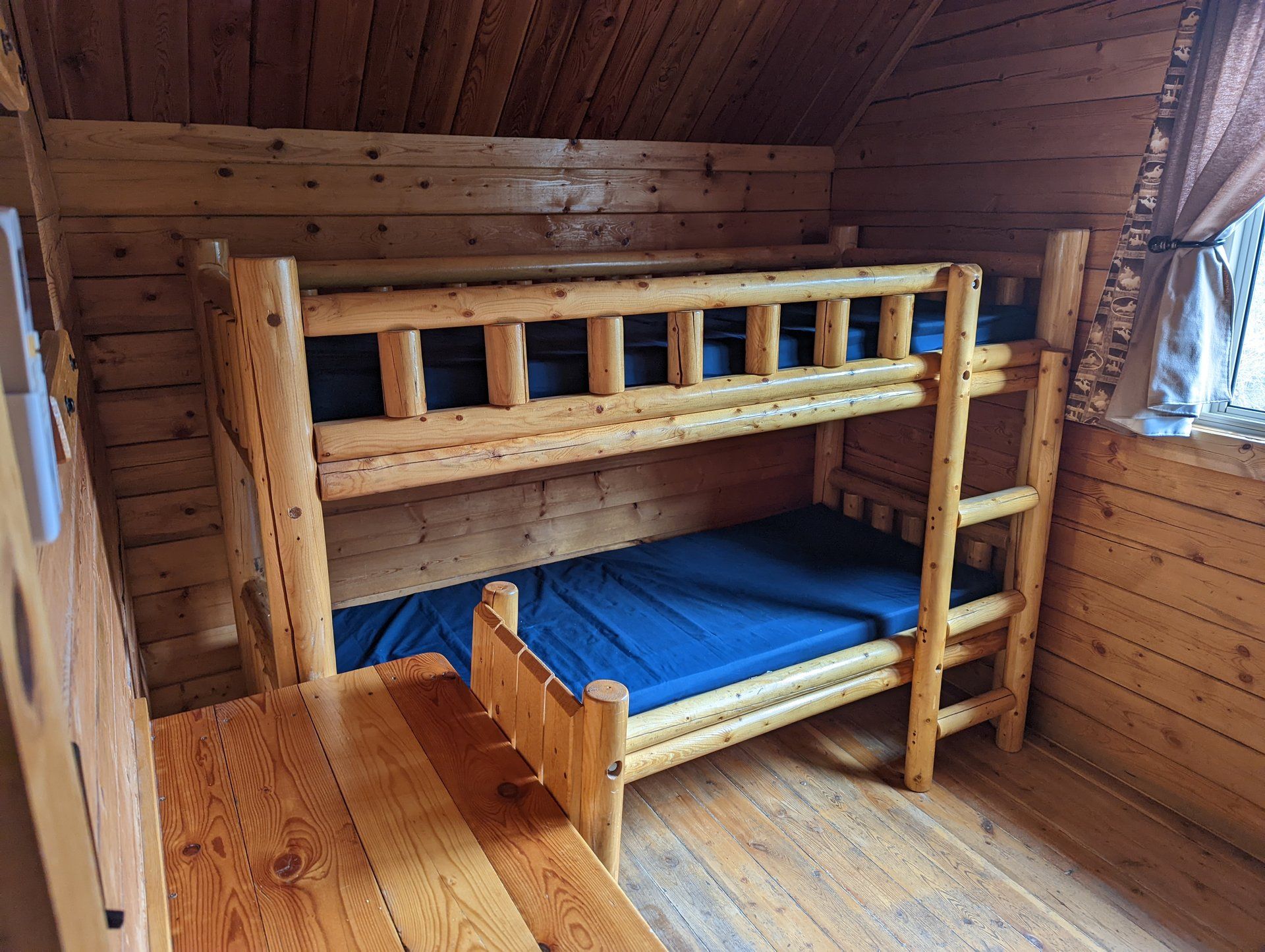 Una cama litera en una habitación tipo cabaña de madera con ventana y mesa de madera.