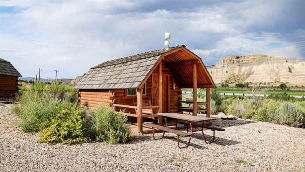 A rustic wooden cabin with a covered porch, a picnic table, and a gravel ground.