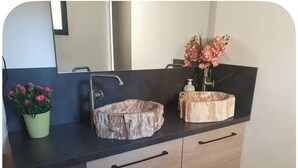 A bathroom vanity with a black countertop, two stone sinks, a mirror, a potted plant, and a vase with flowers. - Room with private Jacuzzi and sea view (Le cannet)