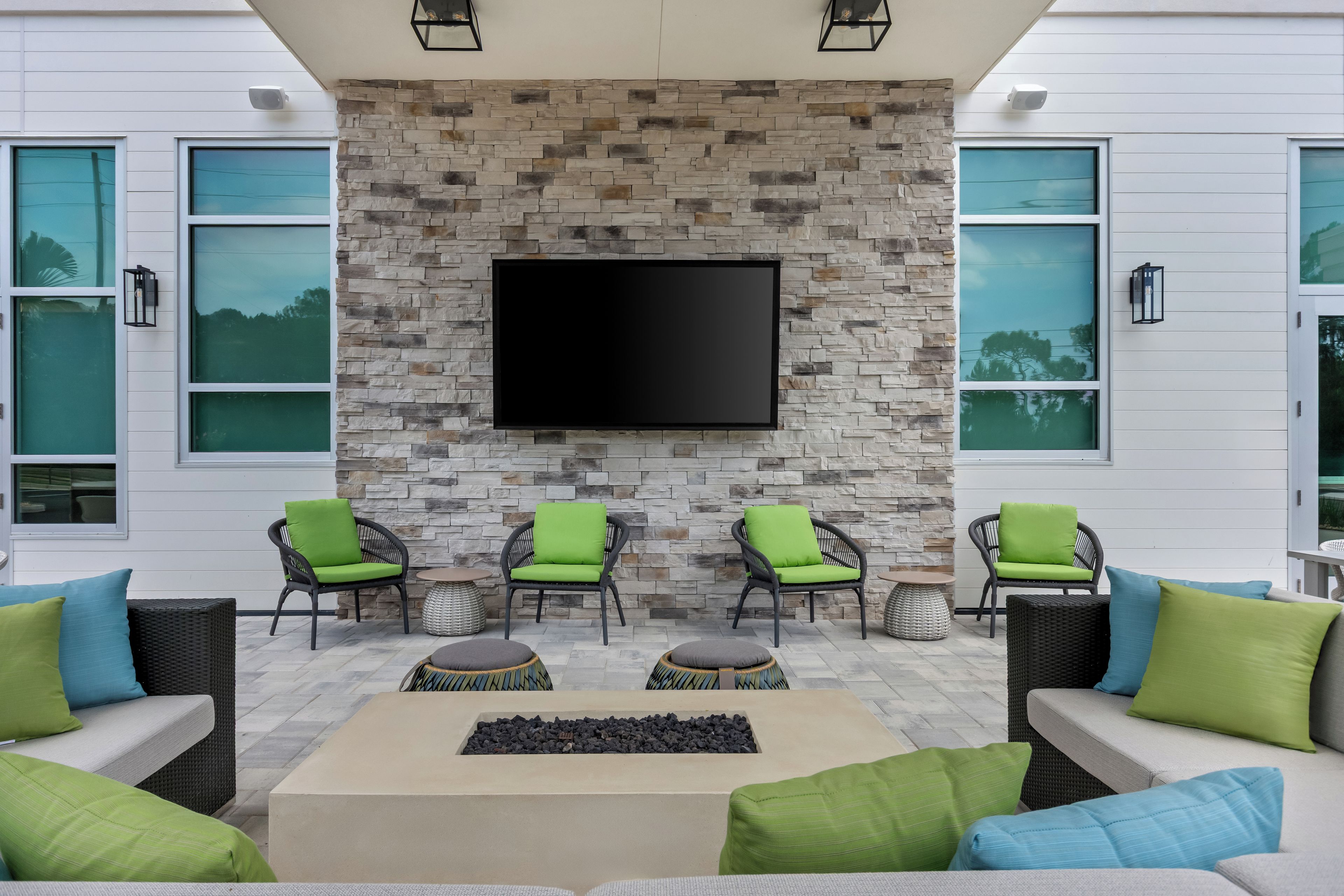 A modern outdoor seating area with stone walls, a flat-screen TV, and green cushioned chairs.