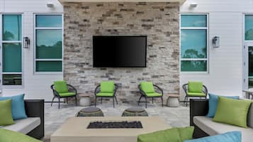 A modern outdoor seating area with stone walls, a flat-screen TV, and green cushioned chairs.