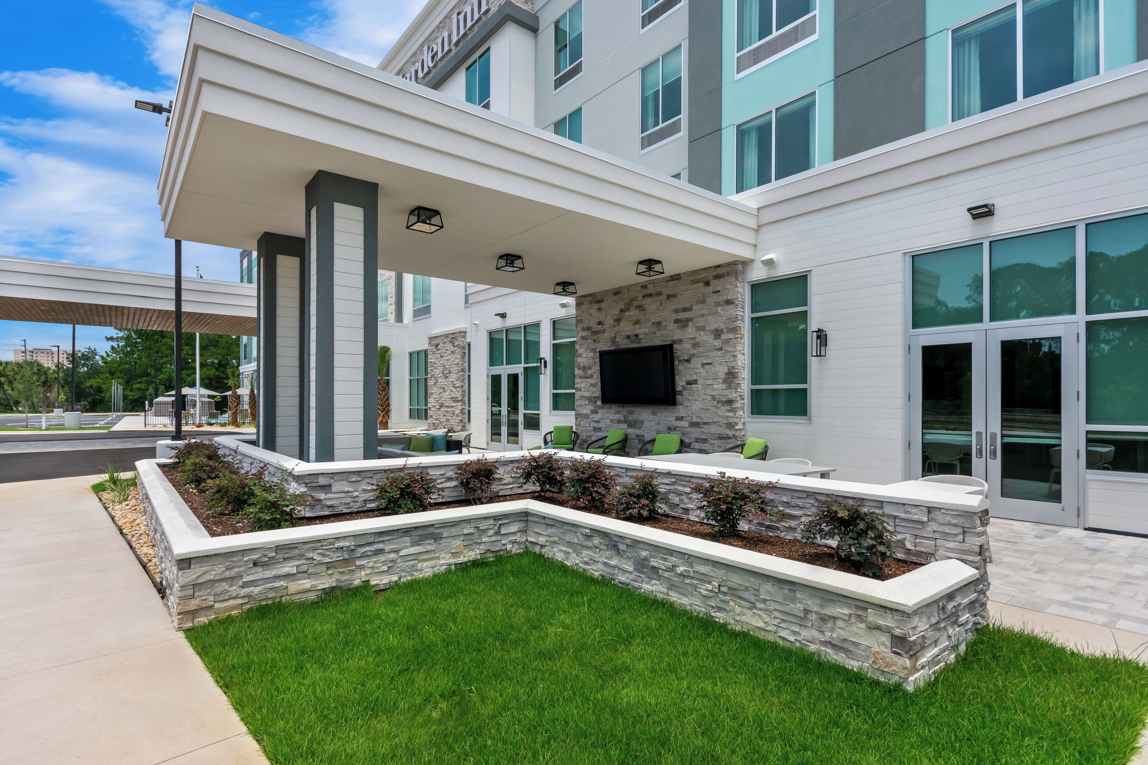 A modern building with a covered outdoor seating area, stone walls, and large windows.