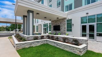 A modern building with a covered outdoor seating area, stone walls, and large windows.