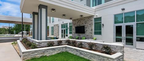 A modern building with a covered outdoor seating area, stone walls, and large windows.
