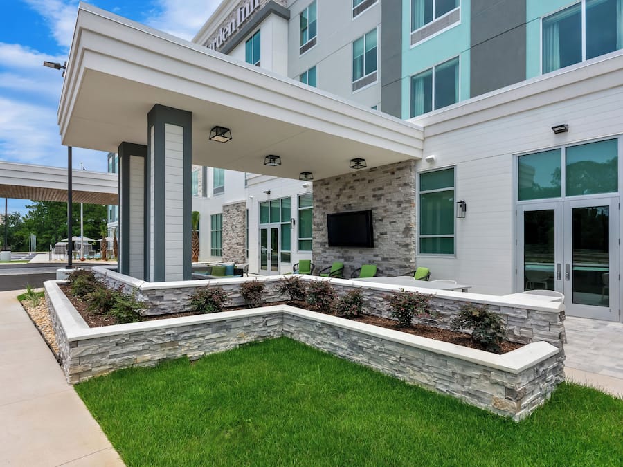 A modern building with a covered outdoor seating area, stone walls, and large windows.