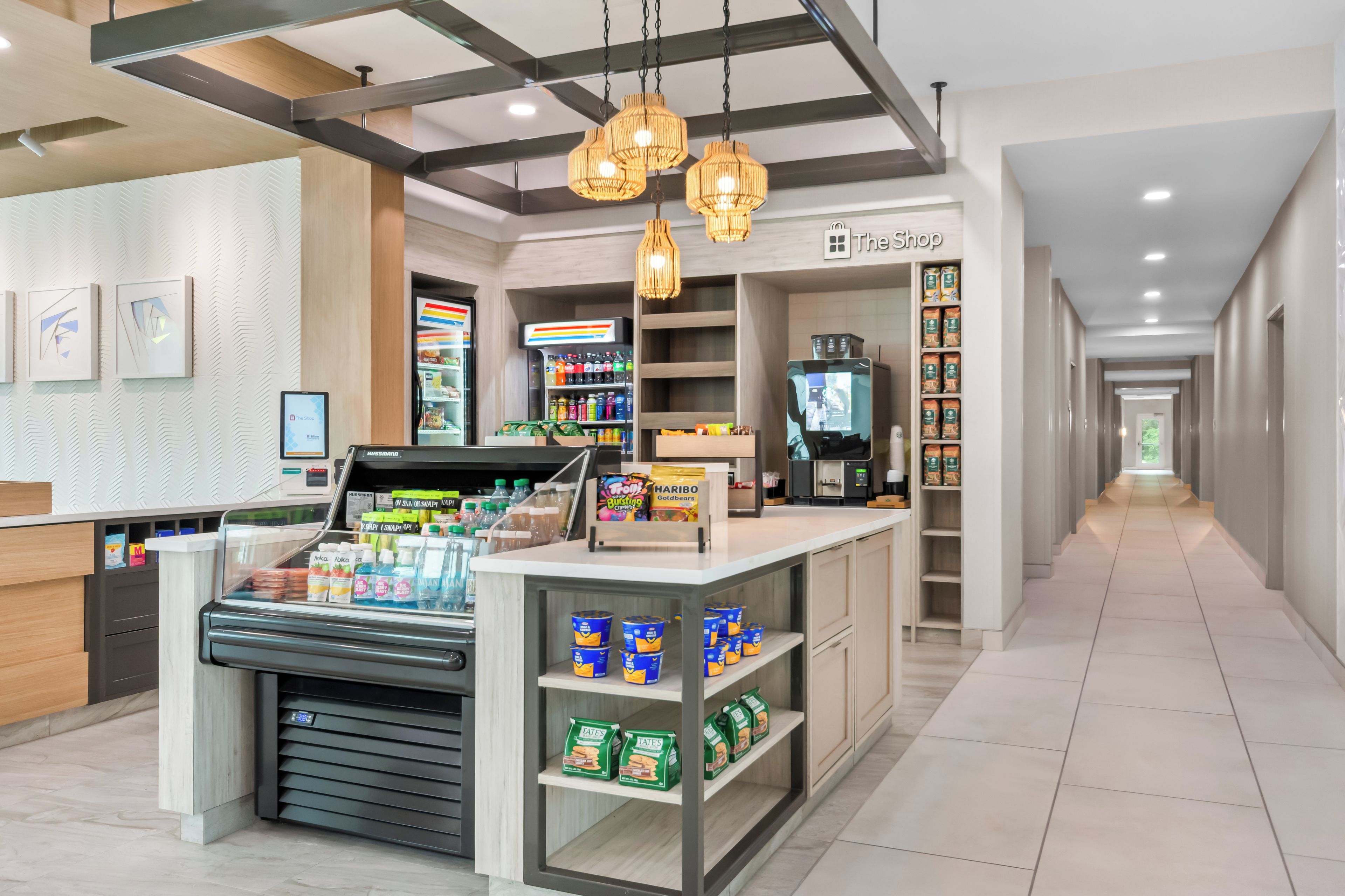 A modern retail area with a checkout counter, shelves stocked with snacks and beverages, and a visible store sign.