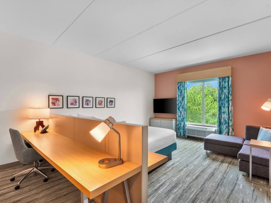 Une chambre d’hôtel équipée d’un bureau, d’une chaise, d’un lit, d’une télévision et offrant une vue sur les arbres par la fenêtre.
