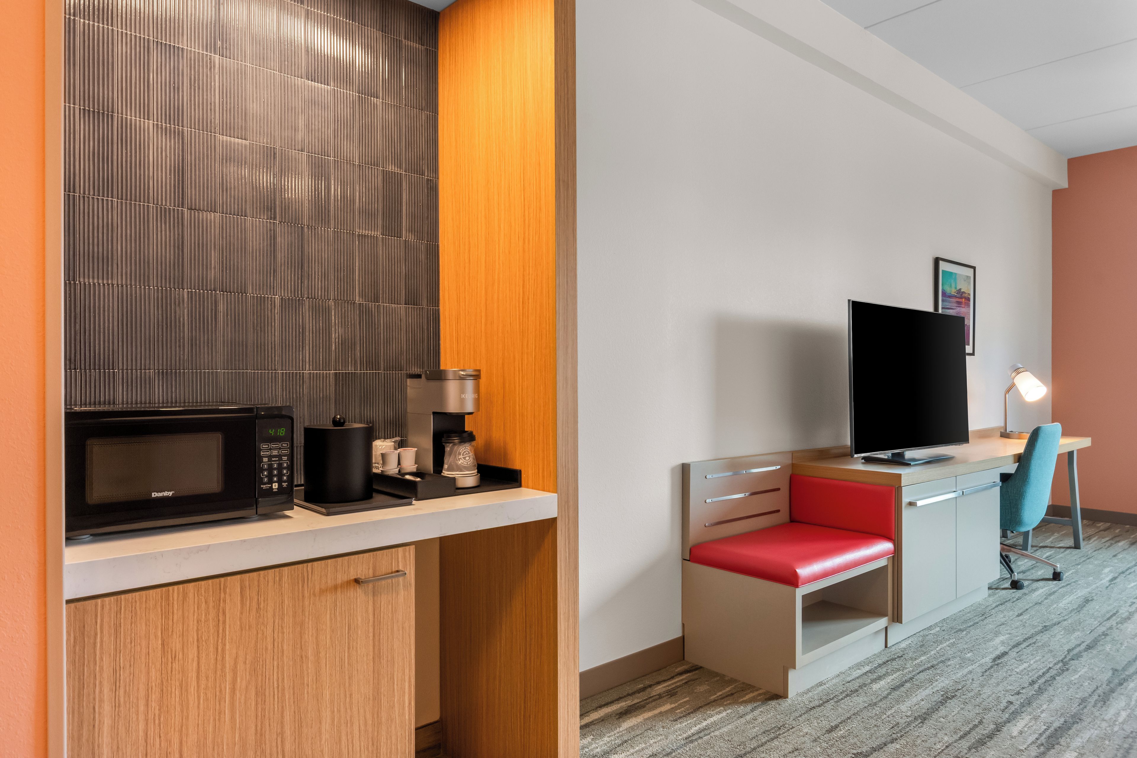 Ein Hotelzimmer mit Küchenzeile, Fernseher, Schreibtisch und Stuhl sowie einem kleinen Fenster.