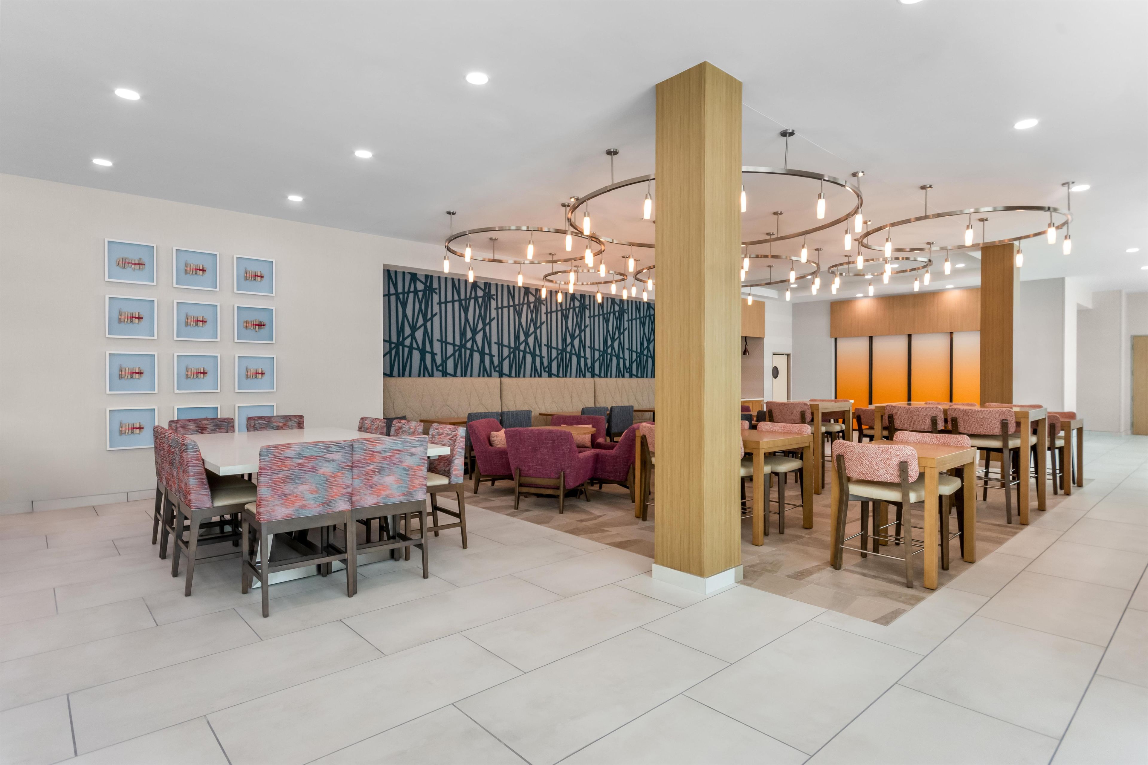 Un espace de restauration moderne, doté de plusieurs tables et chaises, d’un mur décoratif orné de motifs géométriques et d’un plafond agrémenté de luminaires circulaires.