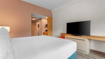 A hotel room with a bed, a television on a wooden desk, and a bathroom visible through an open door.