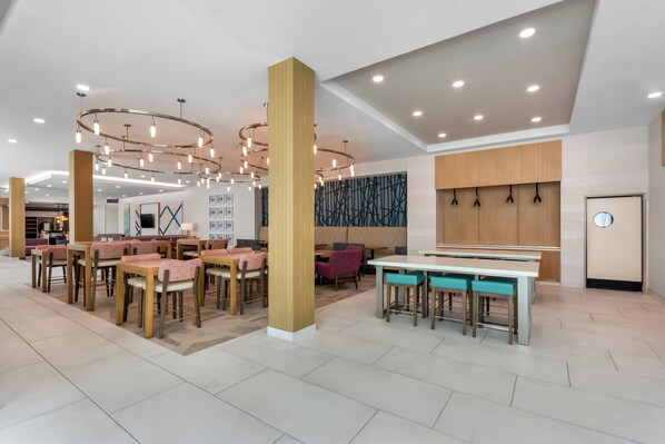 A modern interior with multiple seating areas, including tables and chairs, and a central column. - Hilton Garden Inn Destin Commons (Destin)