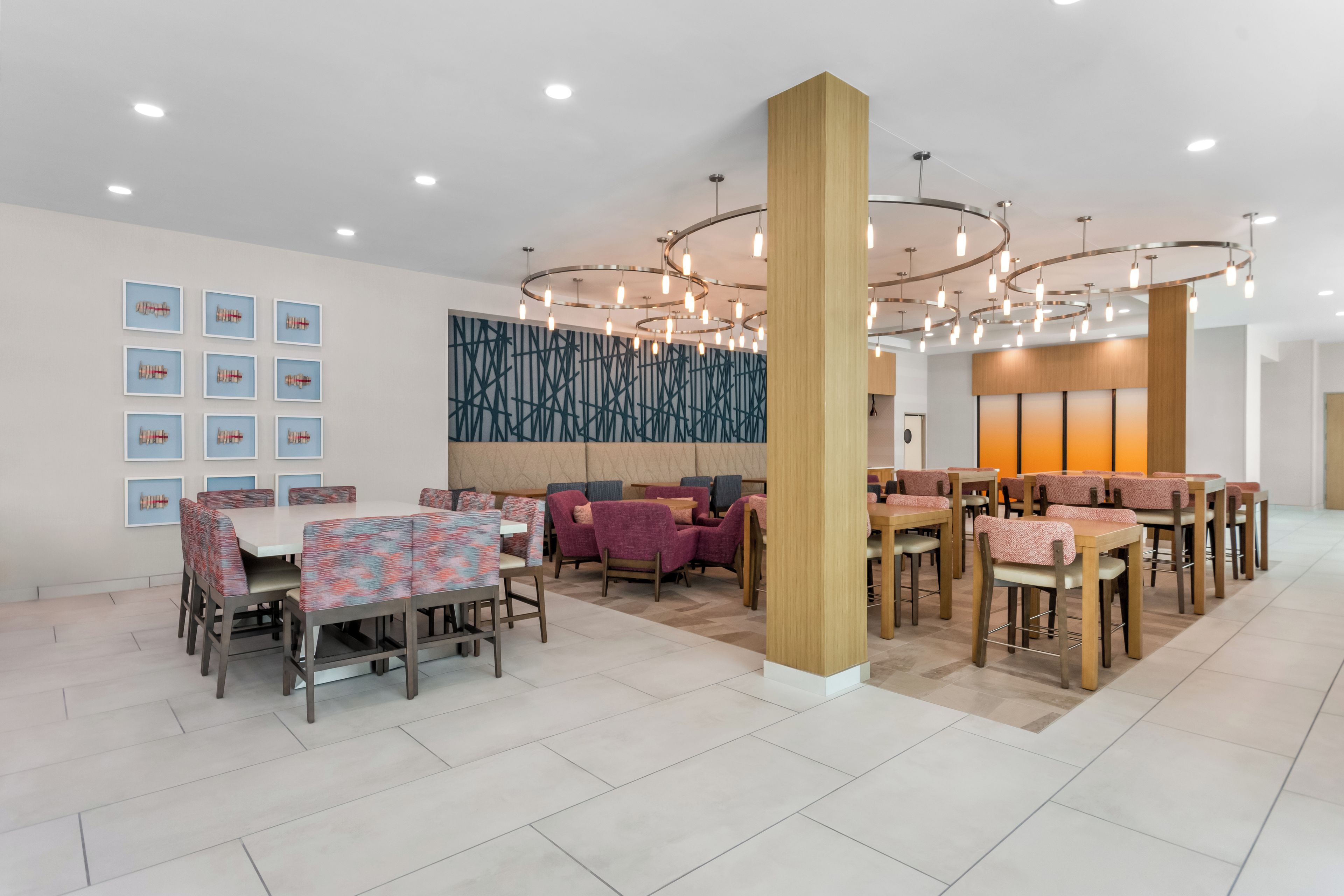 A modern dining area with multiple tables and chairs, a decorative wall, and a ceiling with circular light fixtures.