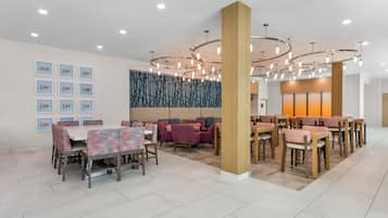 A modern dining area with multiple tables and chairs, a decorative wall, and a ceiling with circular light fixtures.