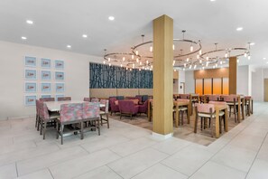 A modern dining area with multiple tables and chairs, a decorative wall, and a ceiling with circular light fixtures.