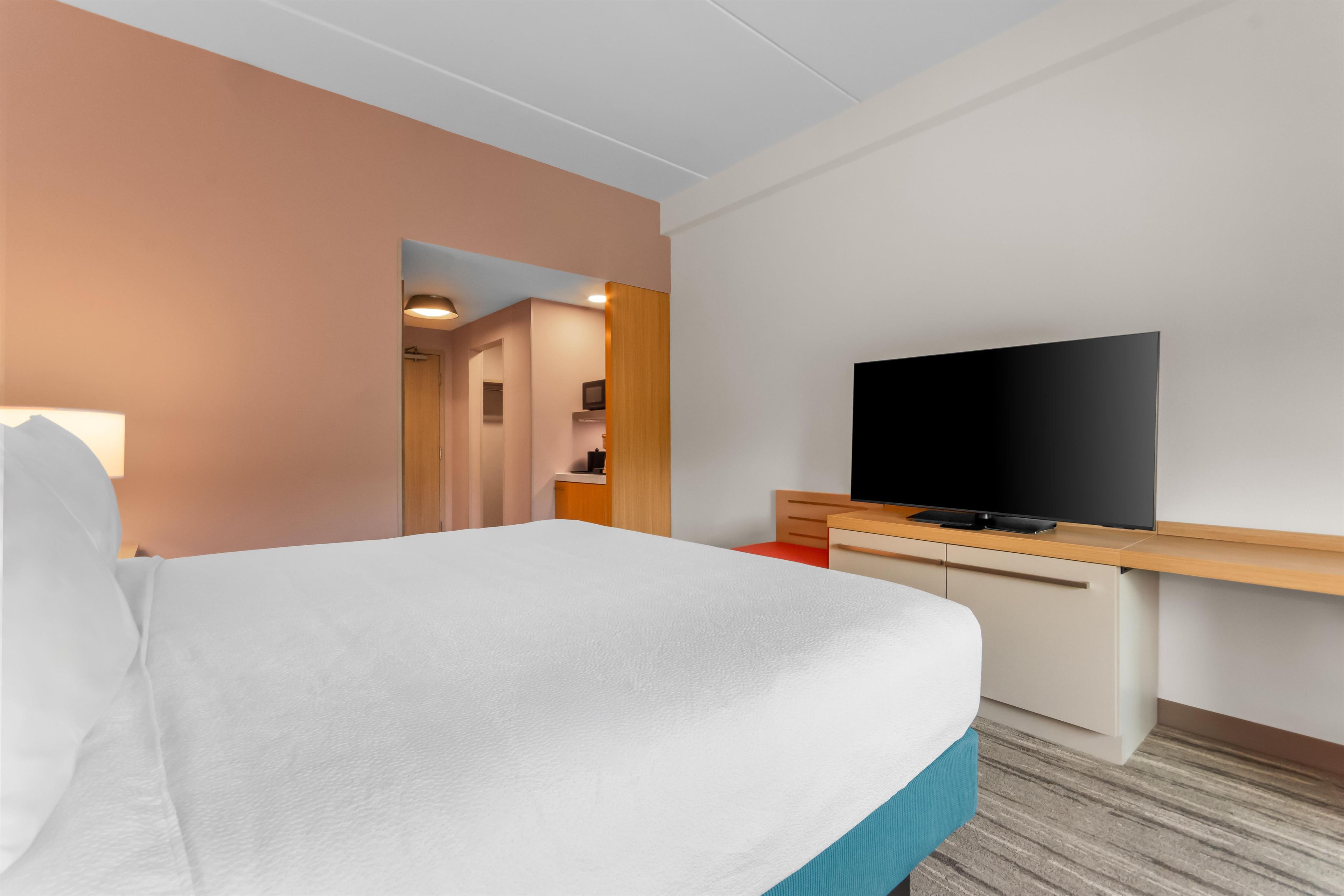 A hotel room with a bed, a television on a wooden desk, and a bathroom visible through an open door.