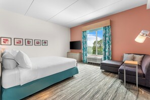 Habitación de hotel con cama, sofá, televisión y ventana con cortinas.