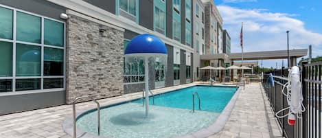 A hotel pool area with a stone wall, a blue water feature, and a flag.