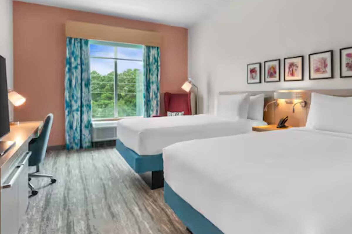 A hotel room with two beds, a desk, a chair, a television, and a window with curtains.