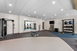 Un gimnasio con equipo de ejercicio variado, una banca y un espejo grande.