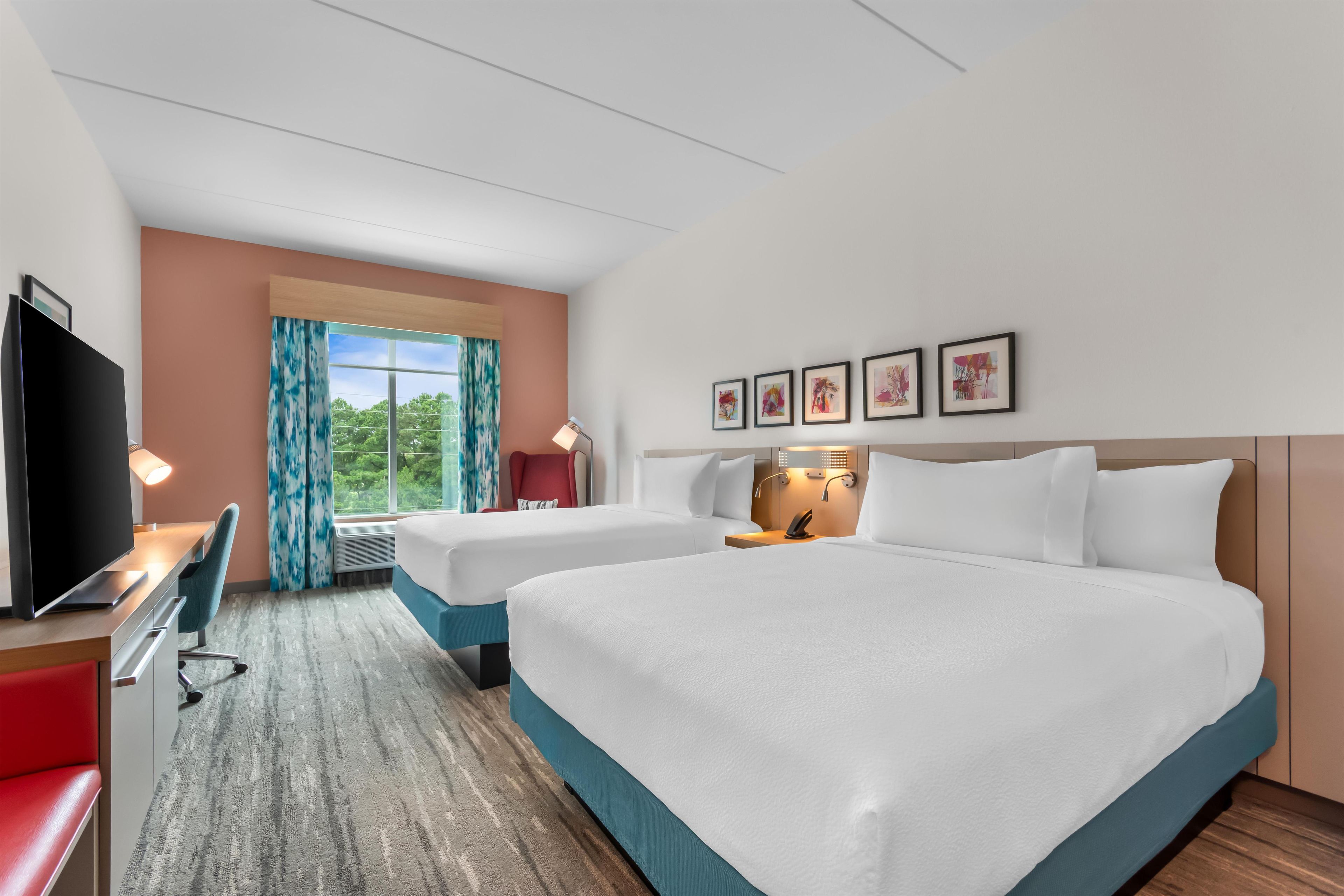 A hotel room with two beds, a desk, a TV, and a window with curtains.