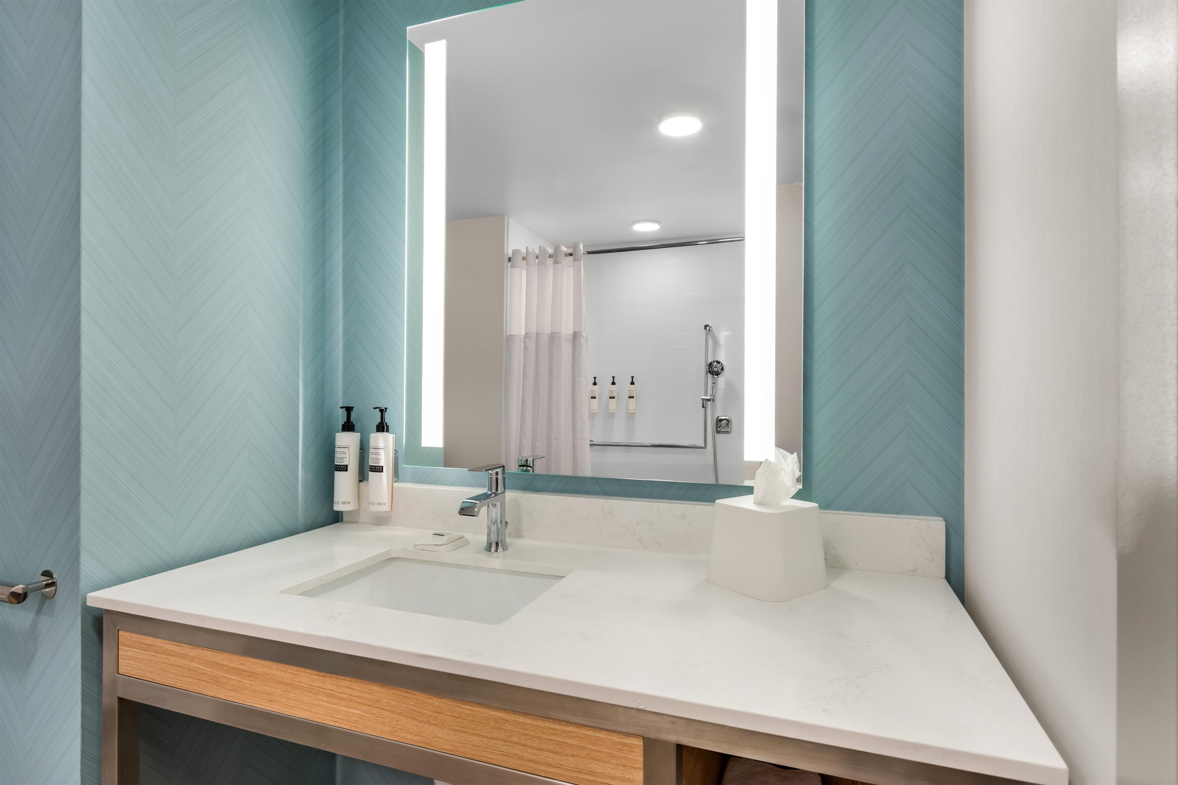A bathroom with a white sink, a mirror, and a shower area visible in the reflection.