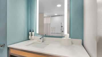Un baño con un lavamanos blanco, un espejo y una zona de ducha.