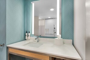 Un baño con un lavamanos blanco, un espejo y una zona de ducha.
