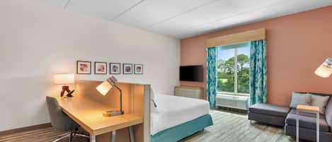 A hotel room with a desk, chair, bed, TV, and a view of the outdoors.