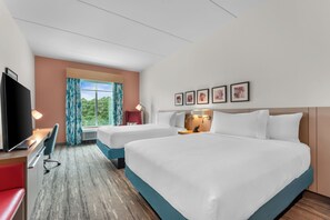 A hotel room with two beds, a desk, a TV, and a window with curtains.