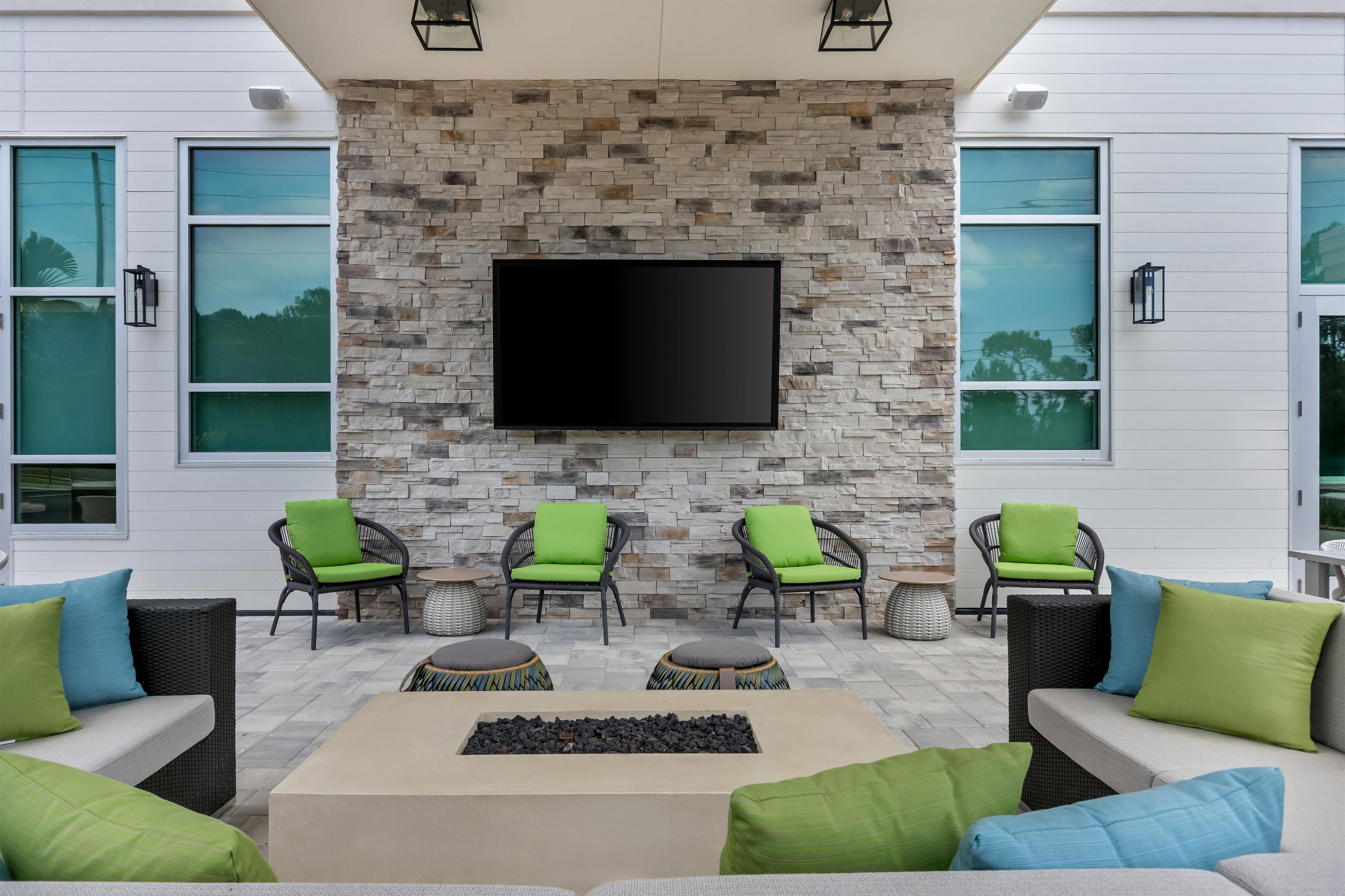 A modern outdoor seating area with stone walls, a flat-screen TV, and green cushioned chairs.