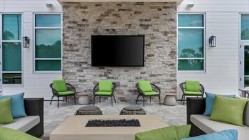A modern outdoor seating area with stone walls, a flat-screen TV, and green cushioned chairs.