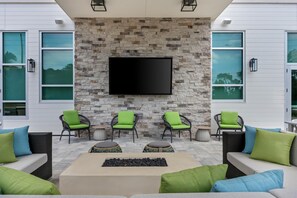 Un espacio al aire libre moderno con paredes de piedra, un televisor de pantalla plana y sillas verdes con cojines.