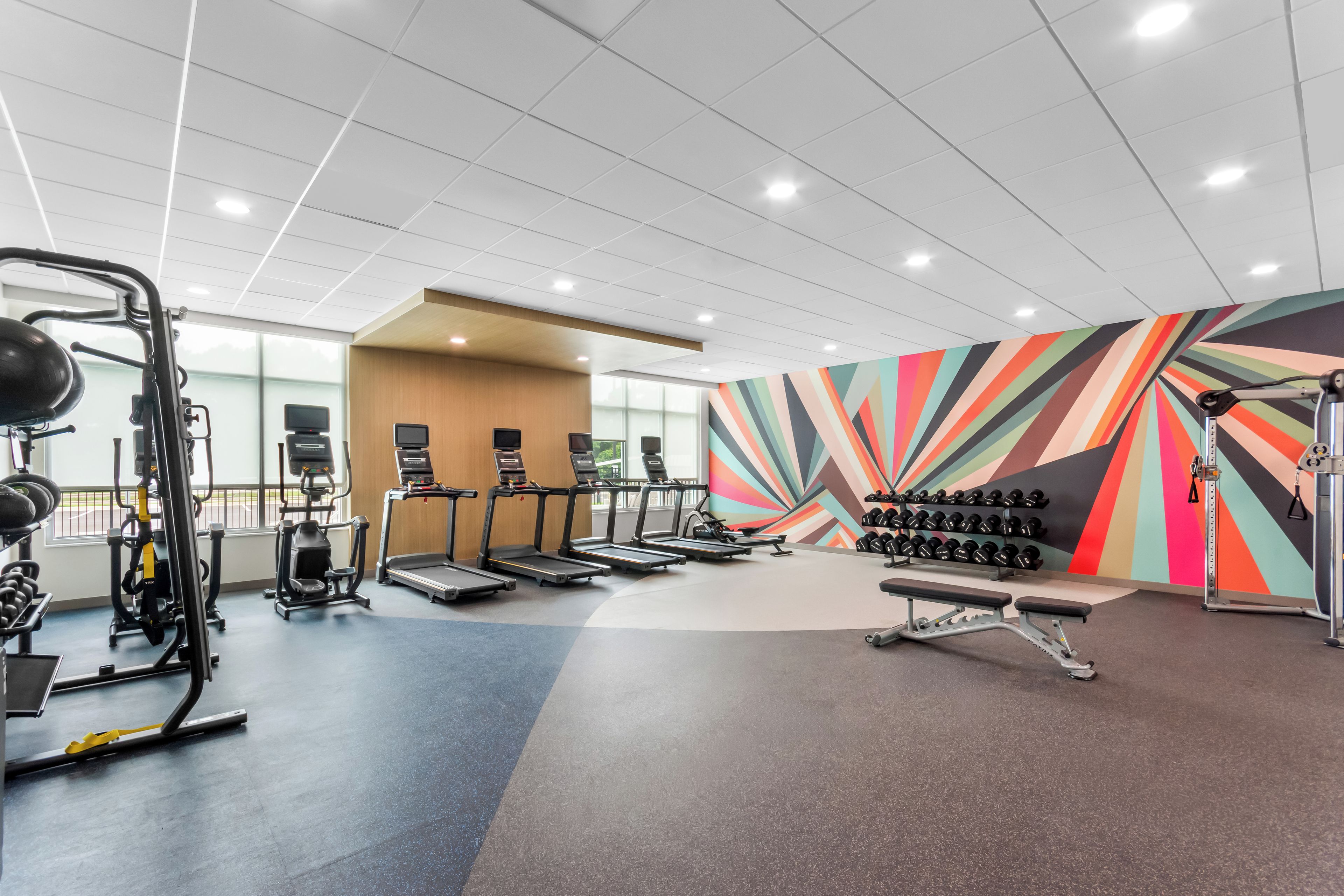 A gym with treadmills, weight machines, and a colorful wall.